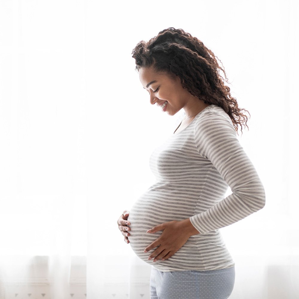 Pregnant, African American woman holding her belly and smiling